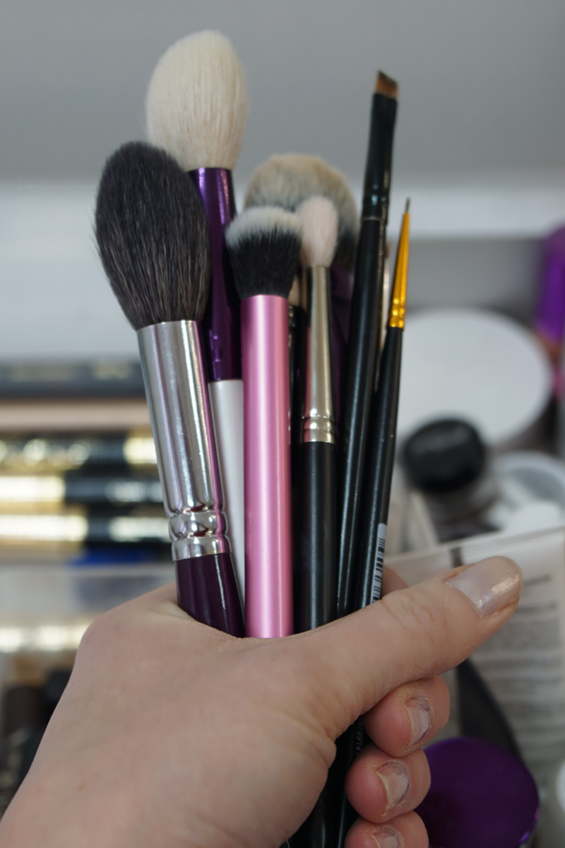 mano con muchas brochas de maquillaje